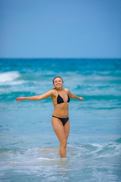 Una ragazzina in costume da bagno verde si trova accanto al mare e ride con le braccia tese