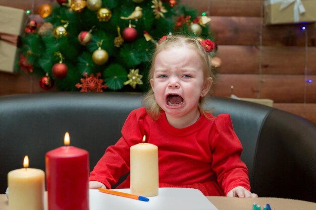 Una ragazzina sullo sfondo decorato albero di Natale scoppiò a piangere e chiama sua madre