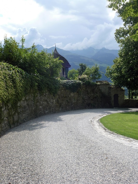 Una recinzione di pietra ricoperta di piante nella prospettiva di una vecchia casa Dietro di lui ci sono le montagne