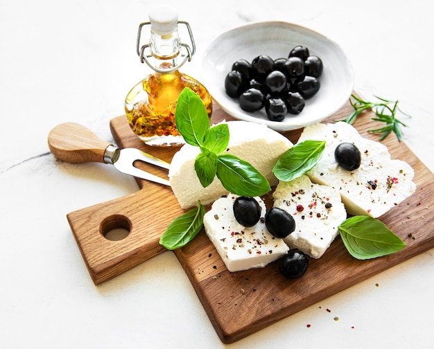 Una ricotta fresca con foglie di basilico e olive su tavola di legno, concetto di cibo italiano