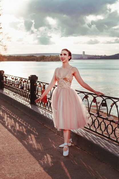 Una ridente ballerina sorridente in un abito di seta rosa posa aggrappata alla recinzione del sentiero