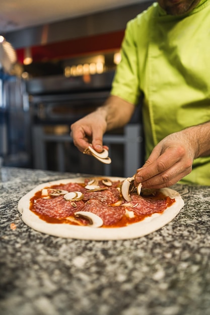 Una ripresa ravvicinata di uno chef che aggiunge funghi alla pizza nella cucina del ristorante