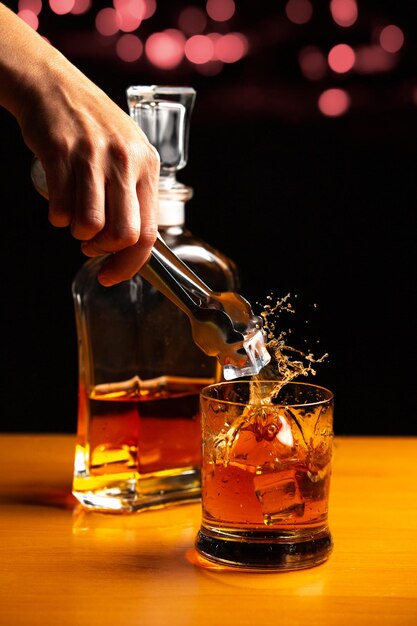 Una ripresa verticale di un barista che mette il ghiaccio e spruzza un bicchiere di whisky in un bar