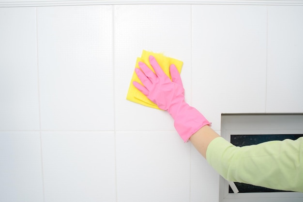 Una rondella di donna sta pulendo la superficie piastrellata in cucina La ragazza con i guanti rosa