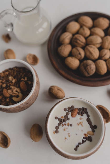 Una sana colazione a base di muesli, farina d'avena, cereali, noci e latte. Tazze con muesli, una brocca di latte, un piatto con le noci