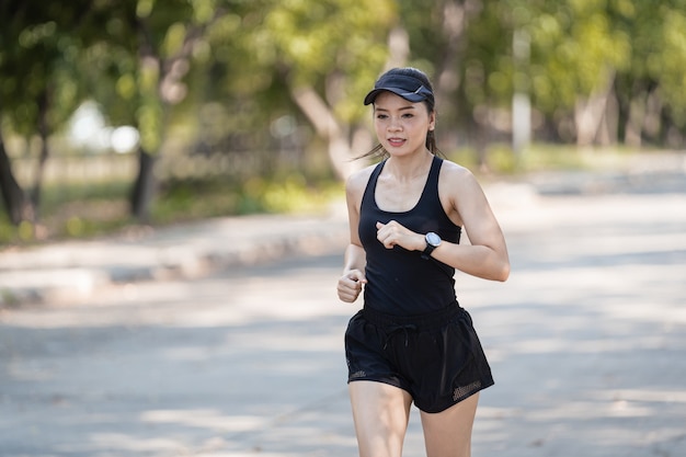 Una sana e felice donna asiatica runner in abiti sportivi neri che fa jogging nel parco naturale della città sotto il tramonto serale