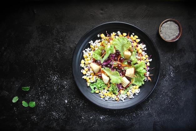 Una sana insalata di frutta e verdura, lattuga, mais, uva, mele sul piatto.