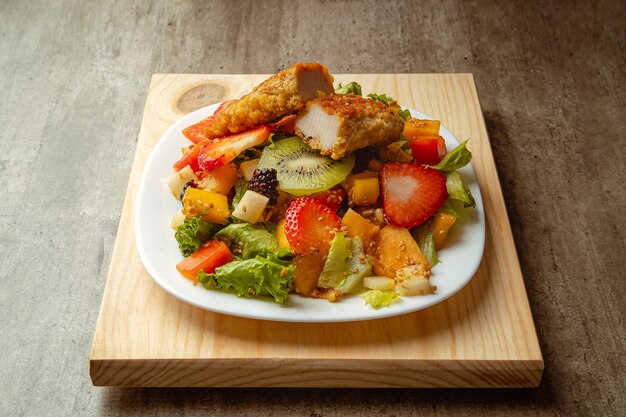 Una sana insalata di frutta fresca con pollo fritto su uno sfondo di legno contiene fragole kiwi e frutti tropicali