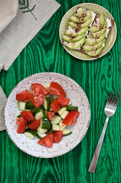 Una sana insalata di pomodori freschi e verdure e un panino fatto in casa con formaggio morbido, avocado e condimento con toast di grano duro. Una colazione salutare.