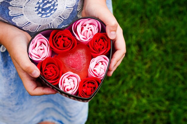 Una scatola in un cuore con rose di sapone nelle mani di una bambina regalo per la festa della mamma regalo d'amore per persone amorevoli data di celebrazione biglietto di san valentino