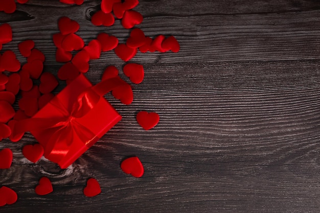 Una scatola rossa con un regalo in piccoli cuori rossi su uno sfondo di legno un modello per il giorno di San Valentino con uno spazio per la copia una cartolina per il 14 febbraio con un posto per il testo Foto di alta qualità