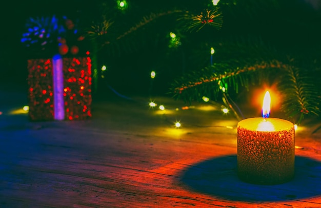 Una scatola rossa di Natale con un regalo e una candela accesa sullo sfondo di un abete naturale con luci di Natale