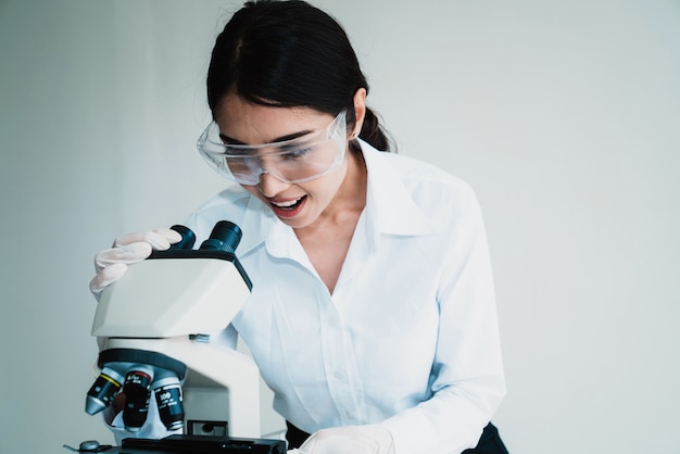 Una scienziata in occhiali protettivi lavora con un microscopio