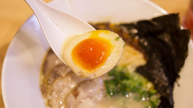 Una scodella di Buta Tonkotsu Ramen Noodles è un grasso brodo di maiale tagliatelle fresche tuorlo d'uovo e tenera pancetta di maiale che si scioglie in bocca Raccogliendo un cucchiaio di tuorlo d'uovo dal ramen