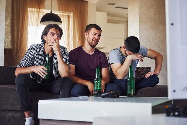 È una sconfitta. Tre amici tristi che guardano insieme il calcio in TV a casa.