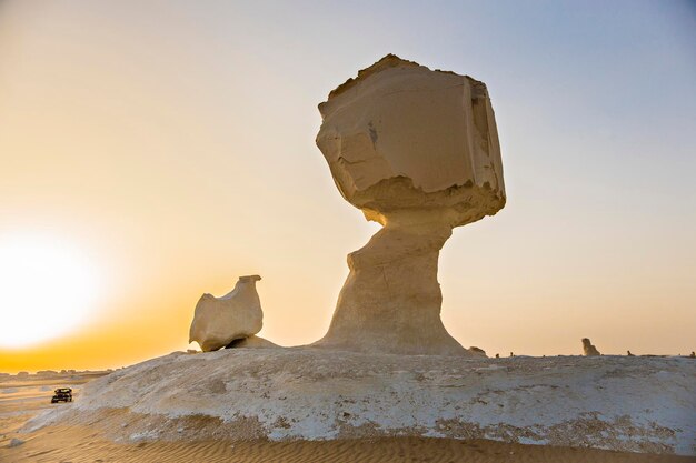 Una scultura di un fungo di pietra si erge su una duna di sabbia.