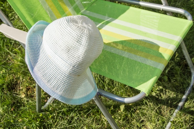 Una sedia da giardino pieghevole vuota per rilassarsi si erge sull'erba verde sul prato in una soleggiata giornata estiva una copia dello spazio un cappello appeso alla sedia