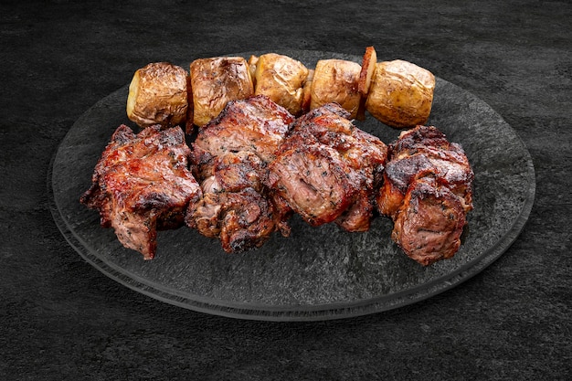Una selezione di carni gourmet grigliate su una tavola di pietra rustica Spiedino di maiale con patate arrostite