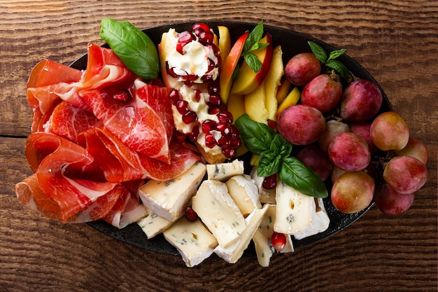 Una serie di antipasti per vino, prosciutto, peperoni, formaggio, uva, pesca su una vista dall'alto del piatto.