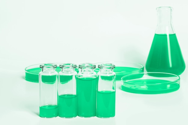 Una serie di barattoli di boccette per il laboratorio con un liquido verde Sullo sfondo di vetreria da laboratorio Piastre di Petri boccette provette Su uno sfondo bianco chiaro