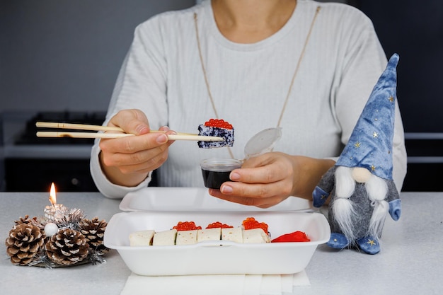 Una serie di panini asiatici in una scatola di plastica a casa in cucina in uno stile festivo La ragazza sta tenendo il cibo con le bacchette Concetto di Natale Decorazioni per il nuovo anno