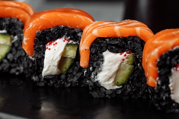 Una serie di rotoli di sushi Philadelphia con pesce rosso, crema di formaggio e riso nero si trova in una barca a piastre