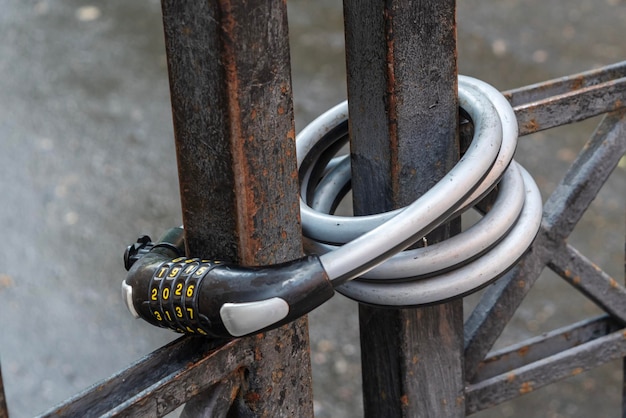 Una serratura codificata in argento e nero è avvolta attorno a un cancello di metallo Il lucchetto della bicicletta sul cancello metallico
