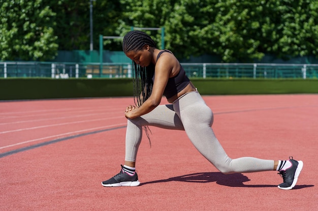 Una signora afroamericana con lunghe trecce si diverte a fare un esercizio efficace per i muscoli gluteali nello stadio della città.