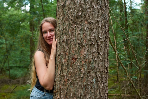 Una signora bionda caucasica con i capelli lunghi che fa sorridere accanto a un albero nella foresta