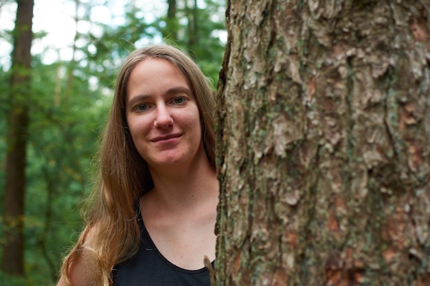 Una signora bionda caucasica con i capelli lunghi che guarda da dietro un tronco d'albero e sorride