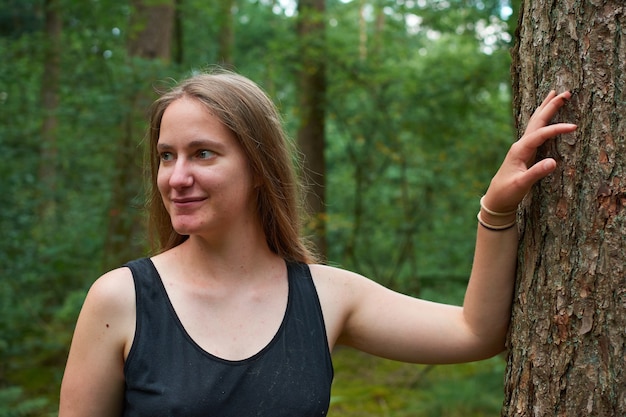 Una signora bionda caucasica con i capelli lunghi in posa accanto a un tronco d'albero nella foresta