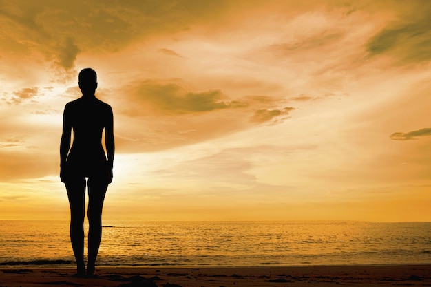 Una silhouette femminile contro un cielo arancione una donna sola guarda il tramonto serale sulla spiaggia vicino