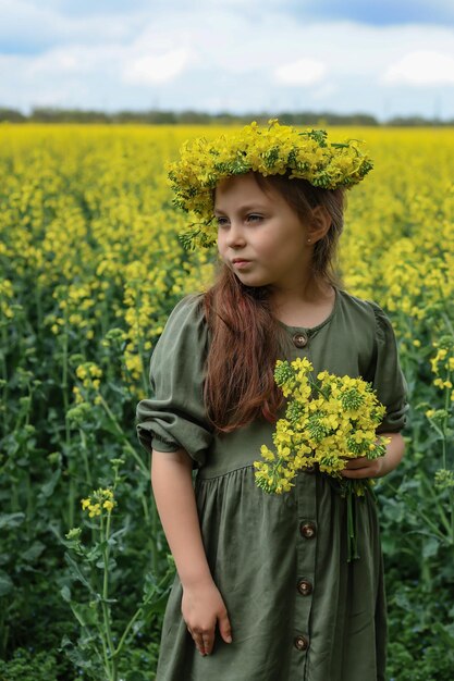 una simpatica bambina di sei anni si trova in un campo di colza con una corona di fiori di colza in testa