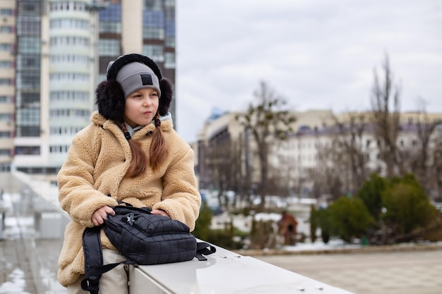 una simpatica bambina di sette anni con uno zaino in mano è seduta sul parapetto della città