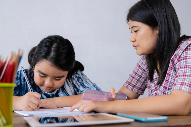 Una simpatica studentessa asiatica che sta studiando a stretto contatto con il suo insegnante sta scrivendo una risposta ponderata