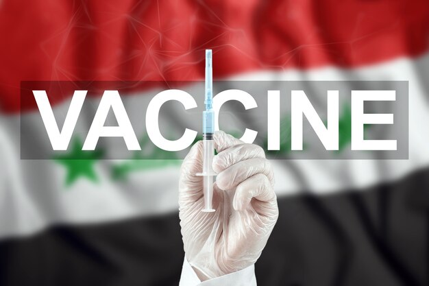 Una siringa con un vaccino nella mano del medico sullo sfondo della bandiera dell'Iraq. Virus corona COVID-19, protezione immunitaria, trattamento contro l'infezione nCoV 2019, vaccinazione.