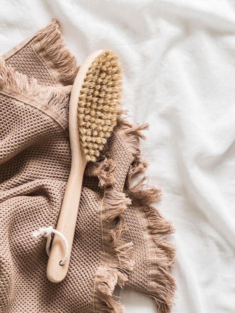Una spazzola da massaggio del corpo asciutto con setole naturali e un asciugamano di cotone beige su uno sfondo bianco