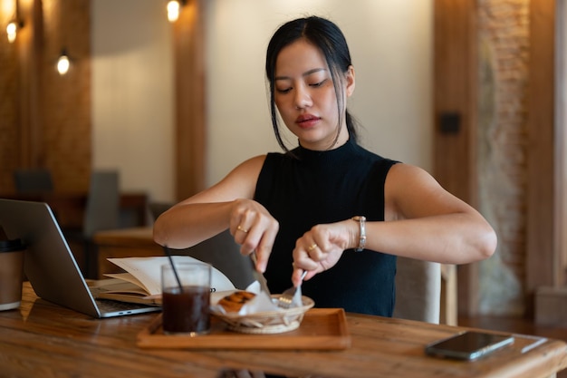 Una splendida donna asiatica sta facendo colazione mentre lavora in remoto in un bar