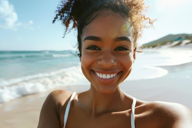 Una splendida giovane donna nera scatta un selfie mentre passeggia sulla spiaggia il suo delizioso sorriso diretto alla telecamera che racchiude l'essenza della tecnologia delle vacanze estive e di uno stile di vita sano