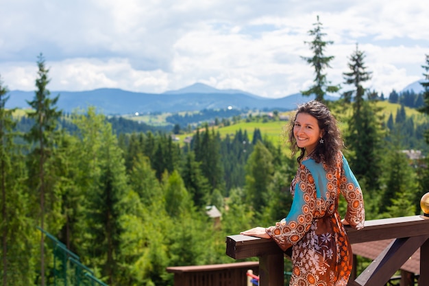 Una splendida ragazza bruna gode della bellezza della natura in piedi sulla terrazza con vista mozzafiato sul paesaggio montano.