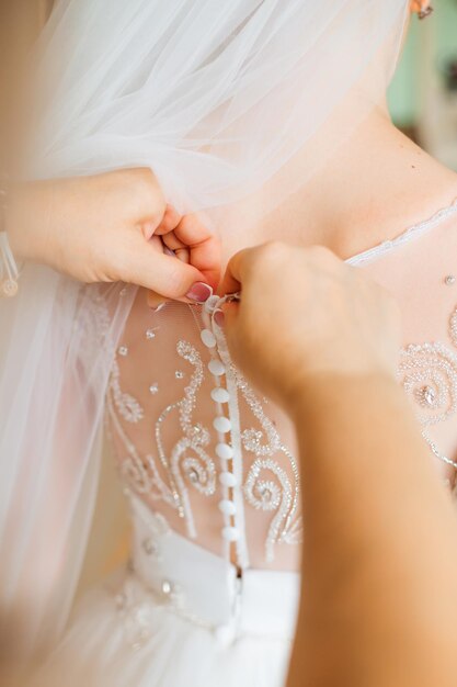 Una splendida sposa in un lussuoso abito bianco si sta preparando per il matrimonio Preparazione del mattino La donna indossa l'abito Vista posteriore