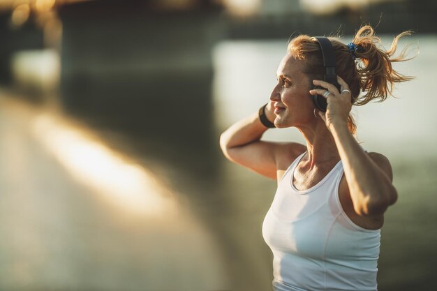 Una sportiva di mezza età che ascolta musica e si prepara ad allenarsi vicino al fiume, in città.