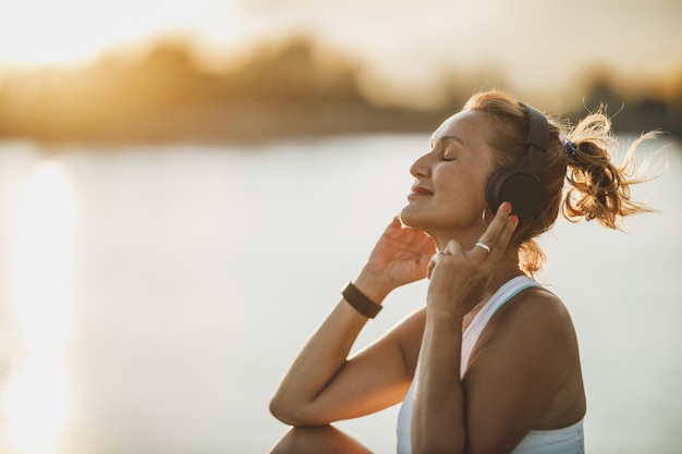 Una sportiva di mezza età che ascolta musica e si prepara ad allenarsi vicino al fiume, in città.