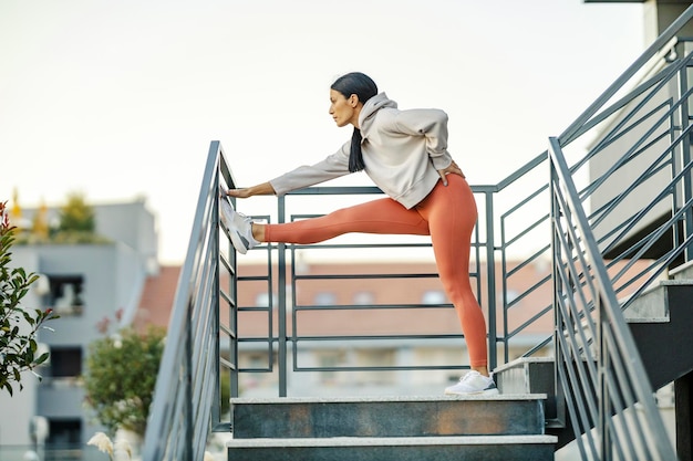 Una sportiva sta allungando le gambe sulla ringhiera mentre si trova sulle scale all'esterno urbano