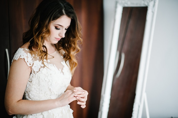 Una sposa attraente in un abito da sposa che indossa e corregge un anello di fidanzamento di nozze d'oro. Preparazioni della sposa. Mattina di nozze.