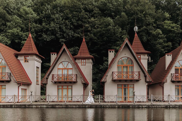 Foto una sposa bruna in un vestito lungo e uno sposo in un abito classico camminano su un ponte vicino a un lago sullo sfondo di un castello riflessione nell'acqua del castello display simmetrico