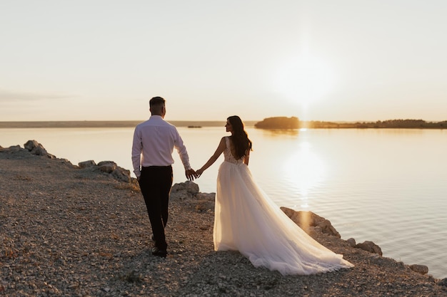 Una sposa e uno sposo camminano sulla spiaggia al tramonto.