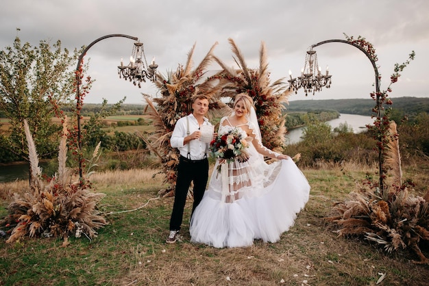 Una sposa e uno sposo posano davanti a un arco floreale con un fiume sullo sfondo.