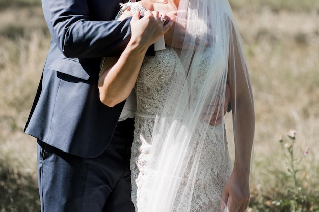 Una sposa e uno sposo si abbracciano davanti a un campo erboso.