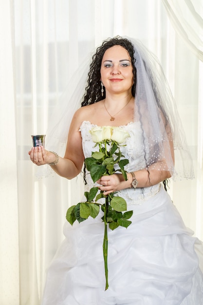 Una sposa ebrea si trova nella sala prima della cerimonia della chuppa con un mazzo di rose bianche tra le mani e un bicchiere di vino